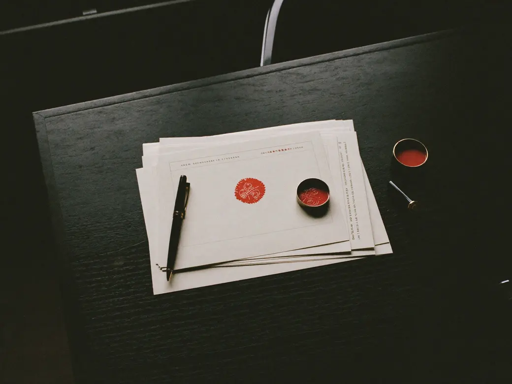 Documentos formales sobre un escritorio, con un sello rojo estampado, pluma y tintero. Imagen ilustrativa.